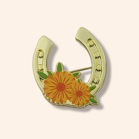 A gold toned horseshoe pin badge with two yellow flowers